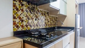 A modern kitchen with a tiled backsplash, a gas stove, a sink, and wooden cabinets. - Spacious Studio Room Apartment at Grand Sungkono Lagoon (Surabaya)