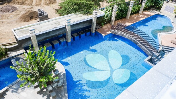 A swimming pool with a blue and white design, surrounded by a concrete deck and stone pillars. - Spacious Studio Room Apartment at Grand Sungkono Lagoon (Surabaya)