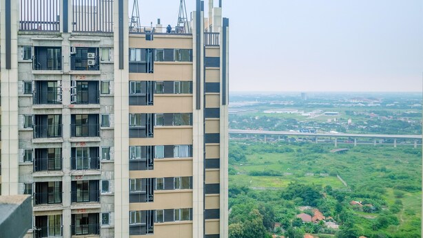A high-rise building with multiple balconies and a view of a bridge and greenery below. - Comfort and Strategic Studio Meikarta Apartment (Cikarang)