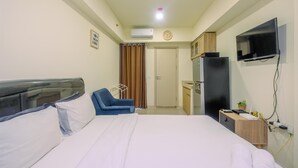 A hotel room with a bed, a desk, a chair, a TV, and a small kitchenette. - Comfort and Strategic Studio Meikarta Apartment (Cikarang)