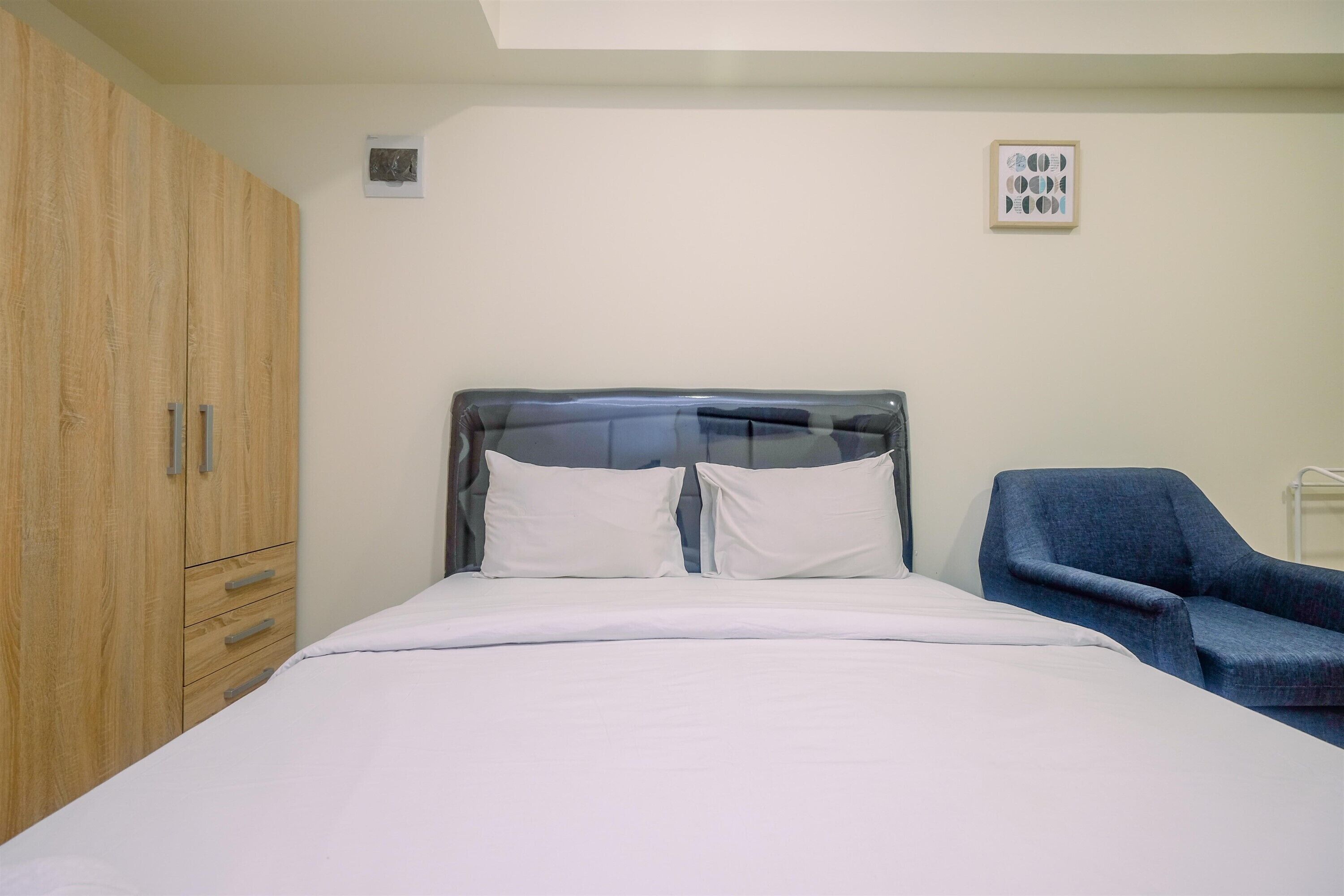 Een slaapkamer met een bed, een houten garderobe, een stoel en een wandlamp.