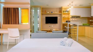 A modern hotel room with a bed, a desk, a chair, a TV, and a kitchenette.