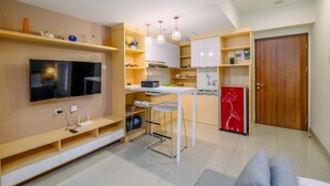 A compact living space with a kitchenette, a dining area, and a TV mounted on the wall.