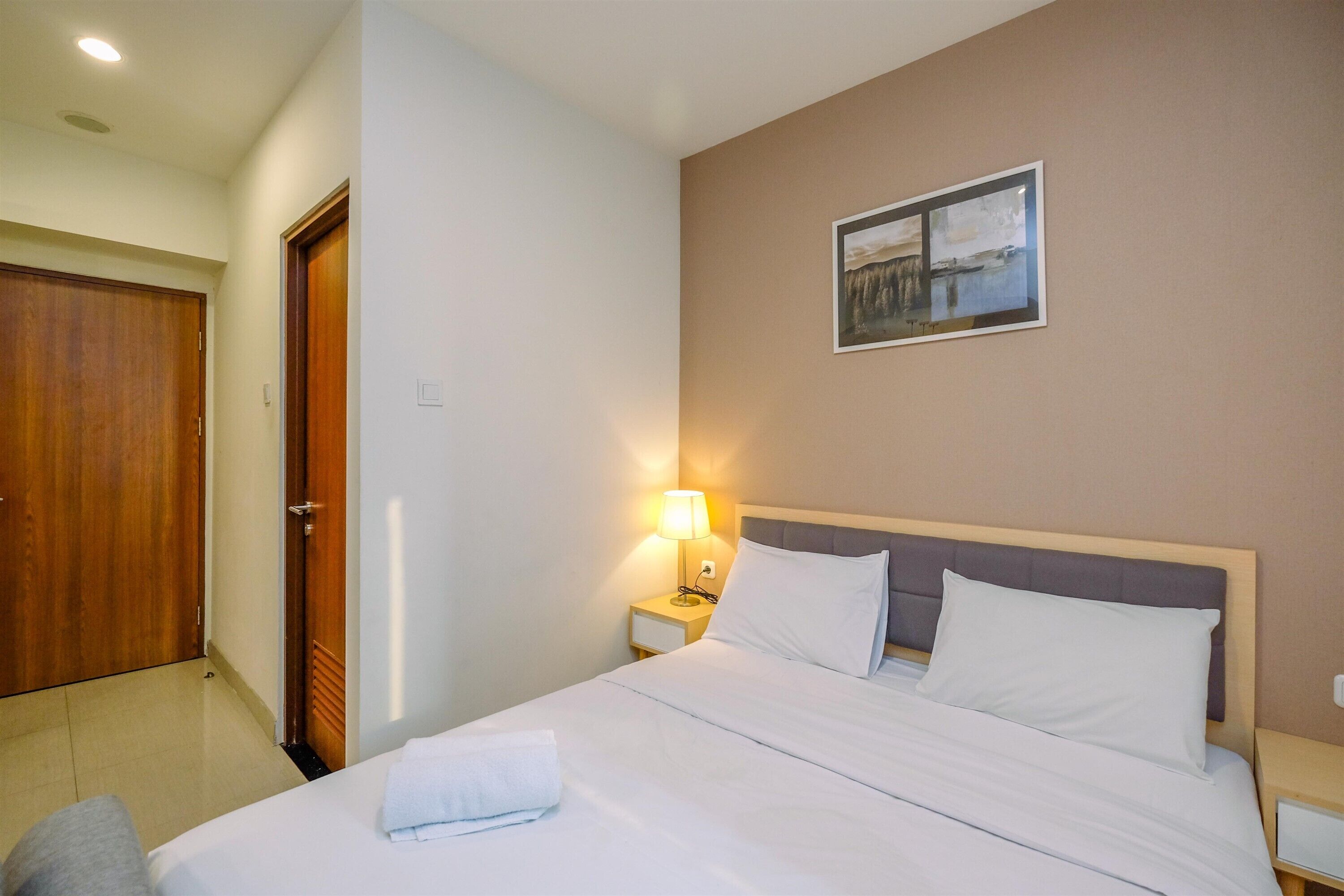 A hotel room with a bed, a nightstand with a lamp, a door, and a painting on the wall.