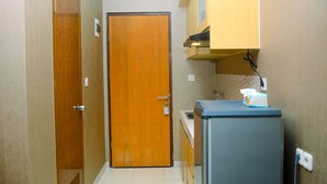 A compact kitchen with a wooden door, a sink, and a refrigerator. - Simply and Cozy Studio at Dave Apartment (Depok)