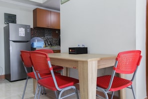 A compact kitchen with a refrigerator, wooden cabinets, and a tiled backsplash. There is a dining table with four red chairs.