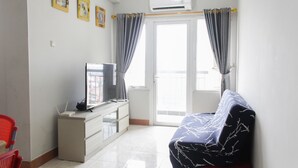 A living room with a sofa, a television, a small table, and a window with curtains. - Comfort and Stylish 2BR at Grand Palace Kemayoran Apartment (Jakarta)