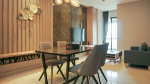 Una sala de estar moderna con una mesa de comedor de vidrio, sillas tapizadas de gris, un televisor de pantalla plana, un sofá y un panel decorativo en la pared.