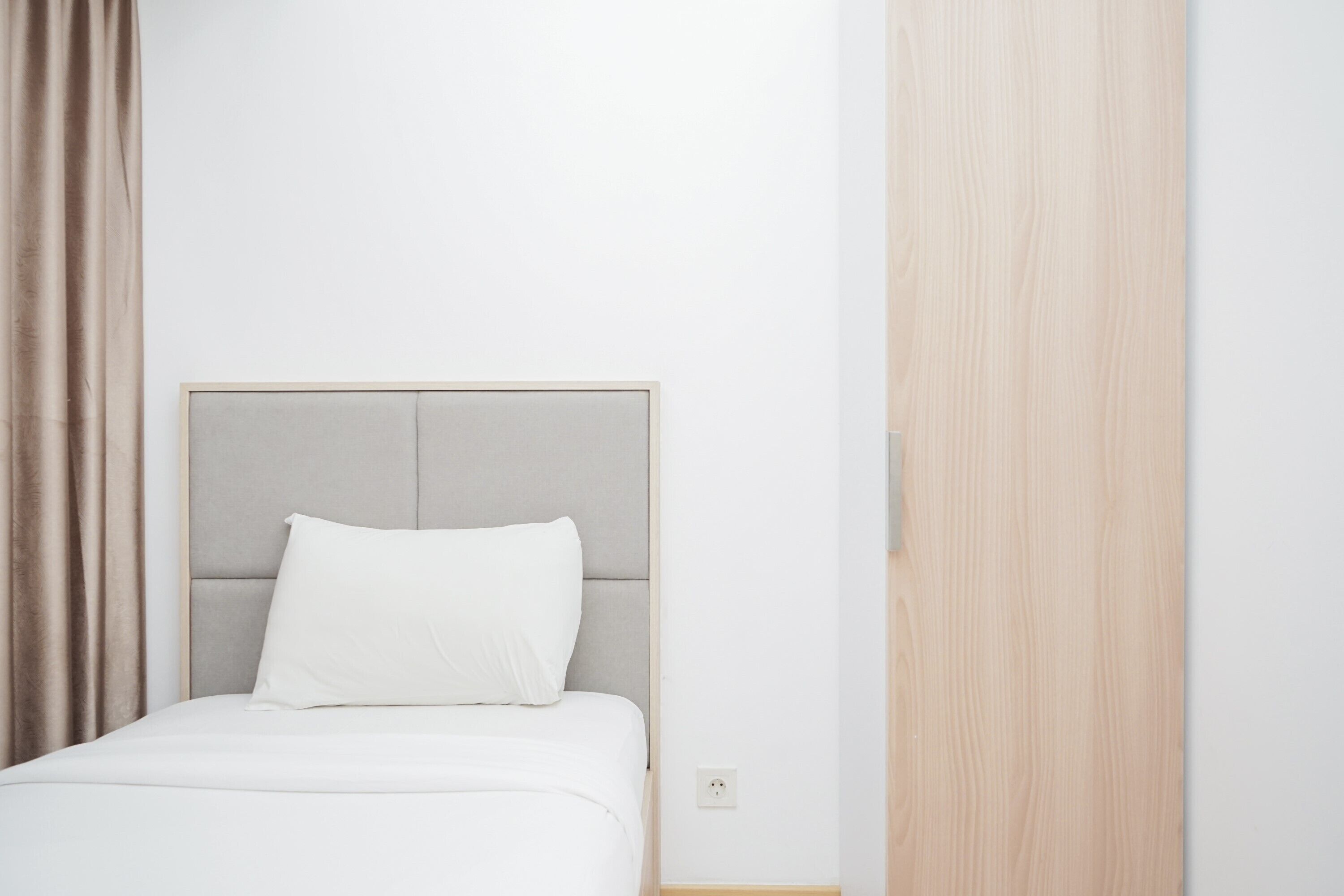 A neatly made bed with a grey headboard and a white pillow in a hotel room.