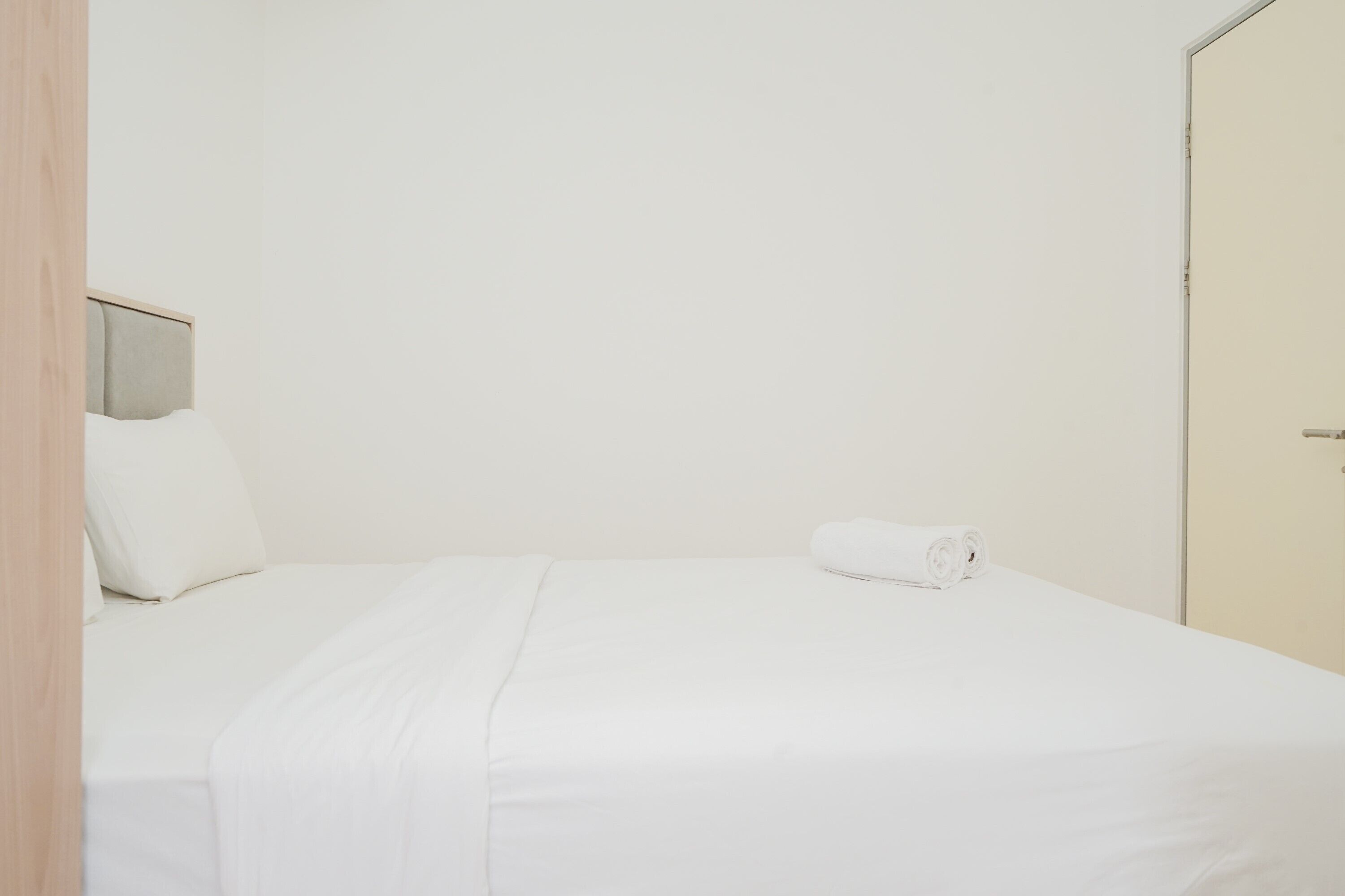 A neatly made bed with white bedding and a rolled towel on the side.