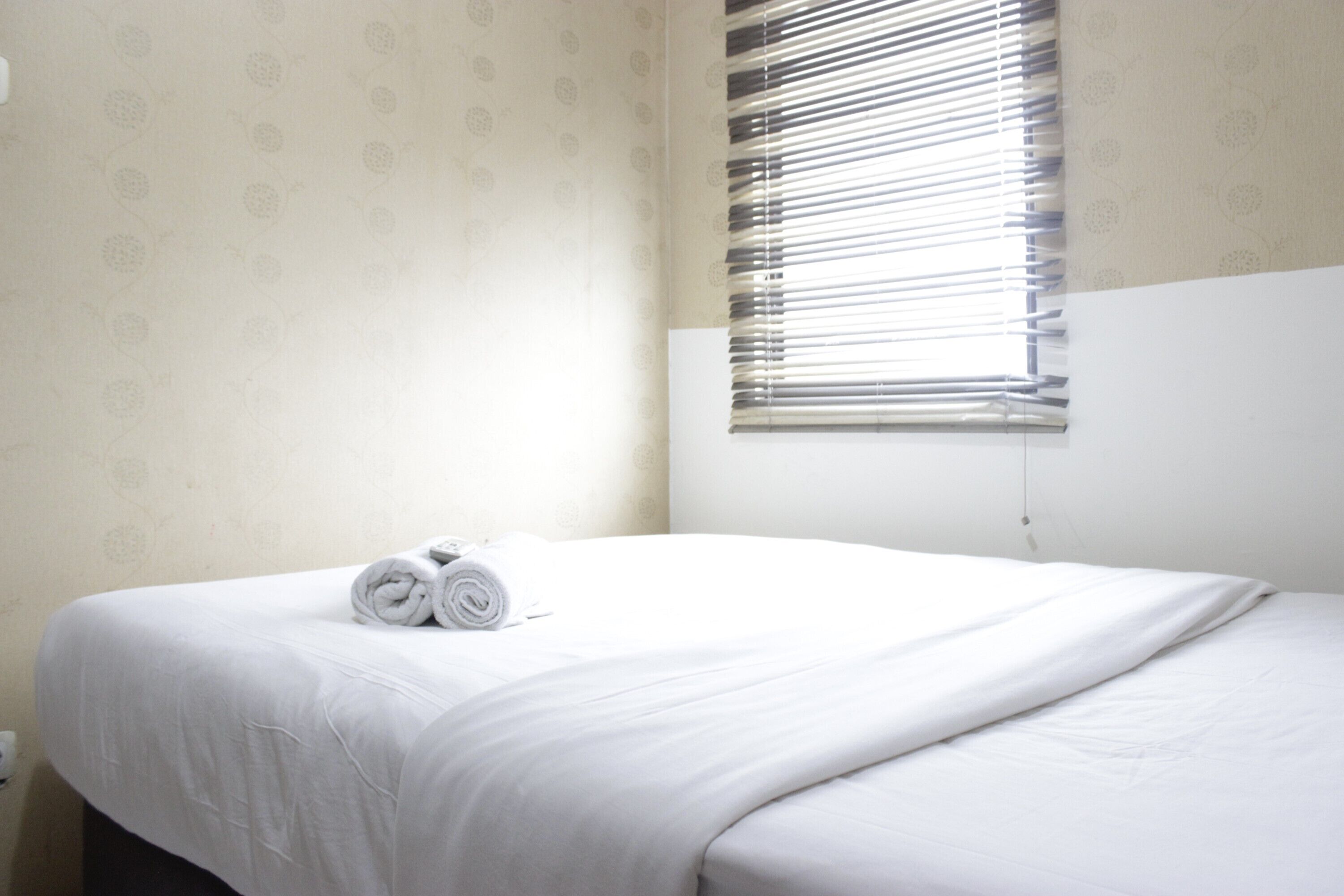 A neatly made bed with white linens and a rolled towel on the side.