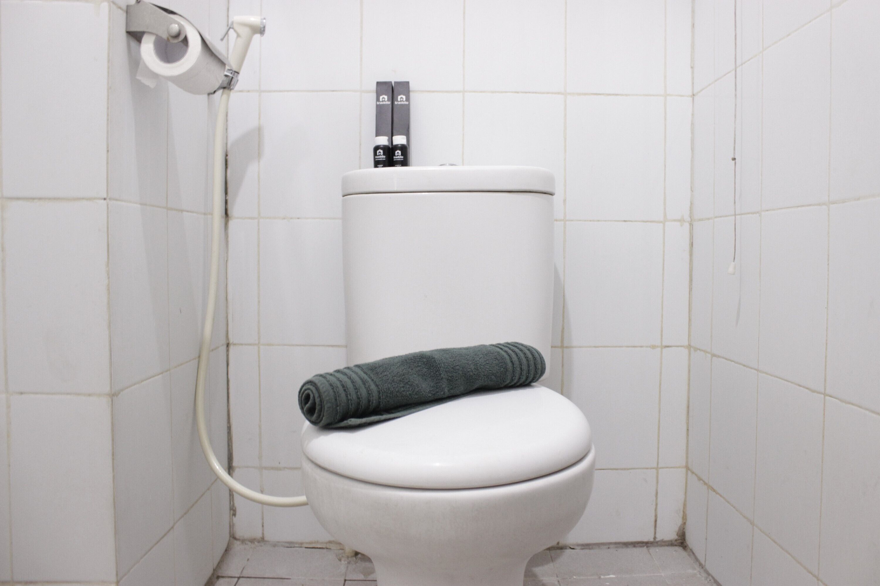 Des toilettes blanches avec une serviette posée sur la lunette et un porte-rouleau de papier toilette fixé sur le réservoir.