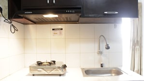 A kitchen with white tiles, a gas stove, a sink, and black cabinets. - Strategic & Relaxing 2BR at Gateway Apartment Ahmad Yani Cicadas (Bandung)