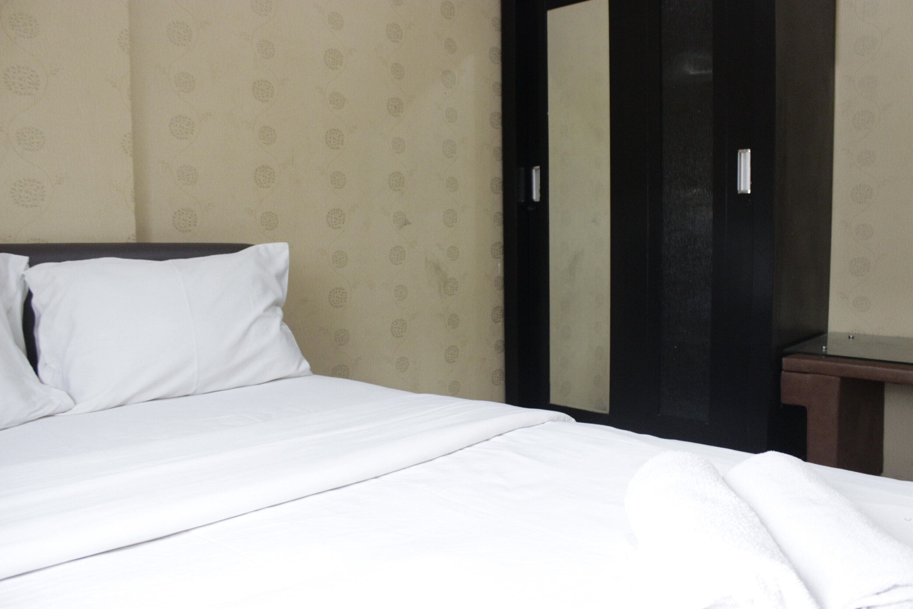 A neatly made bed with white linens in a hotel room.