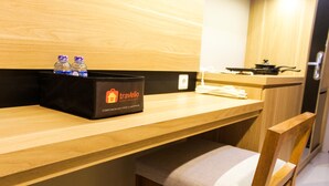 A wooden counter with a black bag labeled 'Travelio' containing bottled water, a wooden chair with a cushion, and a stove in the background. - Cozy and Comfortable Studio (No Kitchen) Apartment at Mustika Golf Residence (Cikarang)