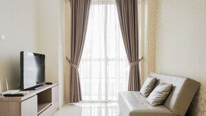 A modern living room with a flat-screen TV on a wooden stand, a beige sofa with cushions, and a large window with sheer curtains. - Wonderful 1BR at Silkwood Apartment (Tangerang)