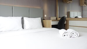 A hotel room with a bed, a desk, a chair, and a mirror. - Favorable 1BR Apartment at Parahyangan Residence near UNPAR (Bandung)