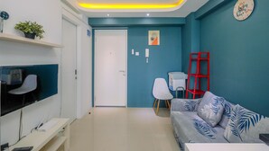 A modern living room with a sofa, TV, and a red ladder against a teal wall. - Clean and Simply Cozy 2BR Bassura City Apartment (Jakarta)