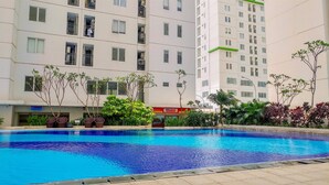 A swimming pool surrounded by a multi-story residential building with balconies and a visible shop sign. - Clean and Simply Cozy 2BR Bassura City Apartment (Jakarta)