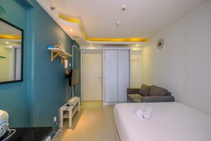 Une chambre d’hôtel comprenant un lit, une télévision, un bureau avec un ordinateur, une armoire et un petit coin salon.