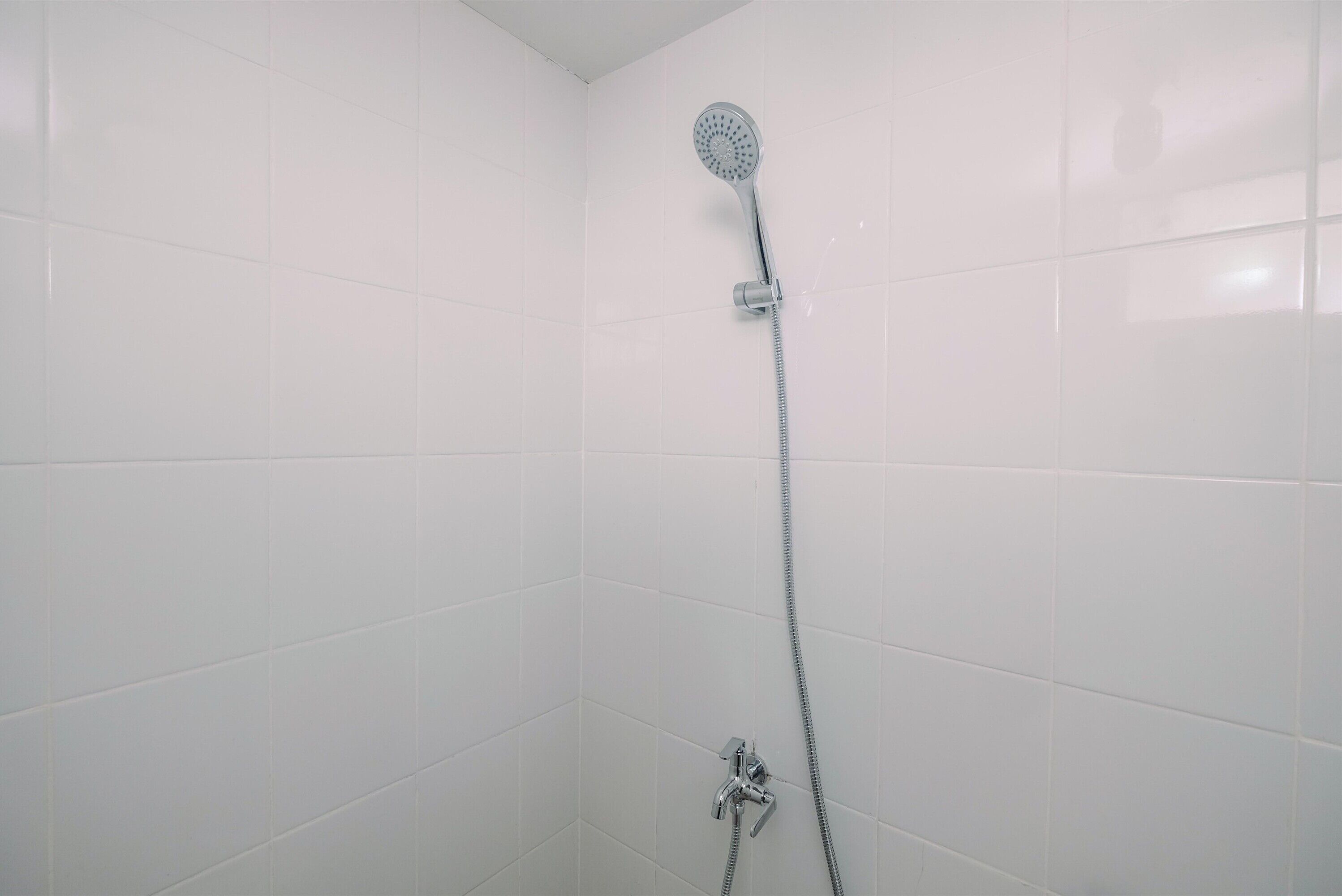 Una ducha con cabezal de ducha de mano y grifo empotrado en un baño con azulejos.