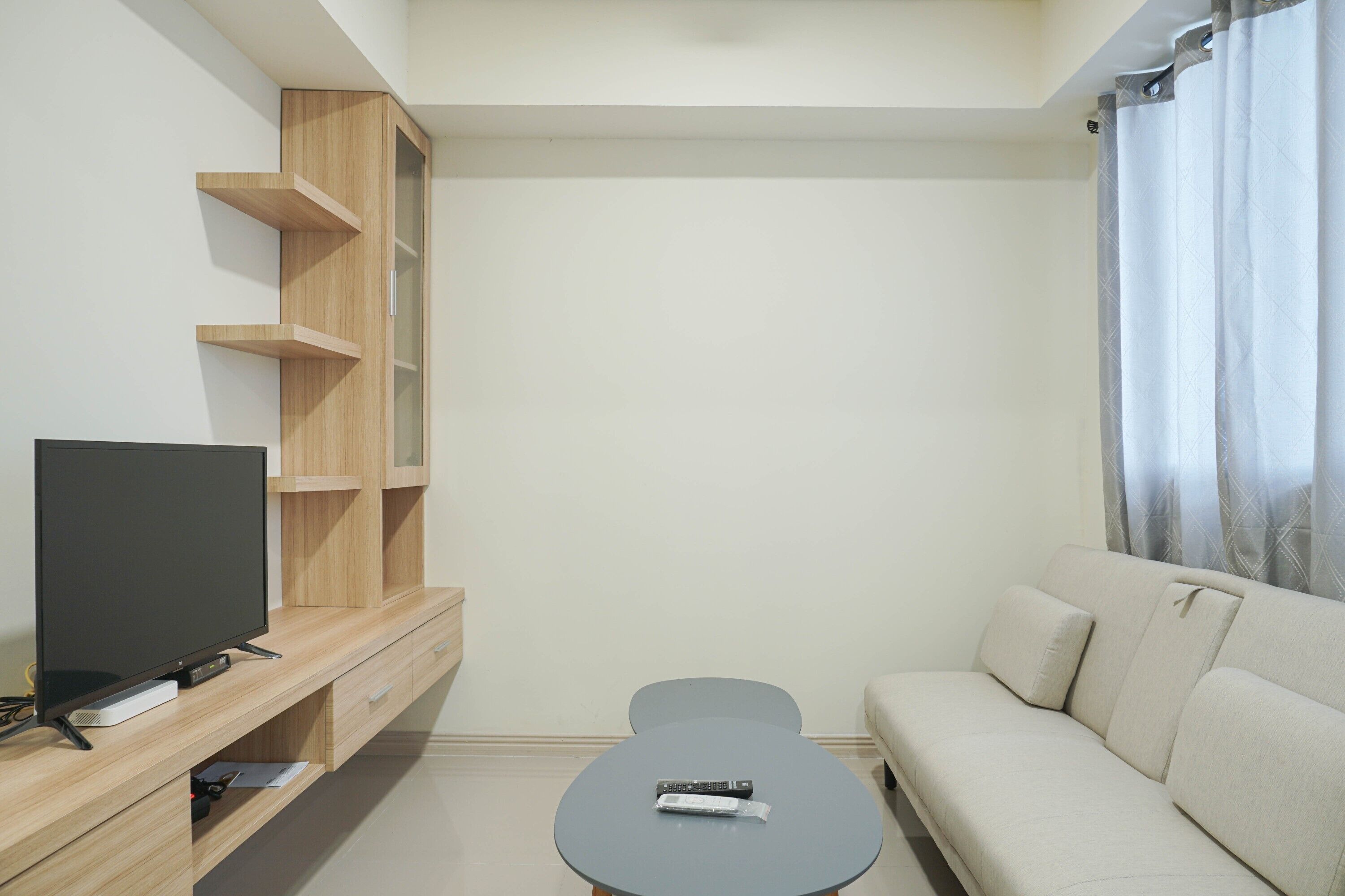 A modern living room with a flat-screen TV, a small table with a remote control, a sofa, and a wooden entertainment unit.