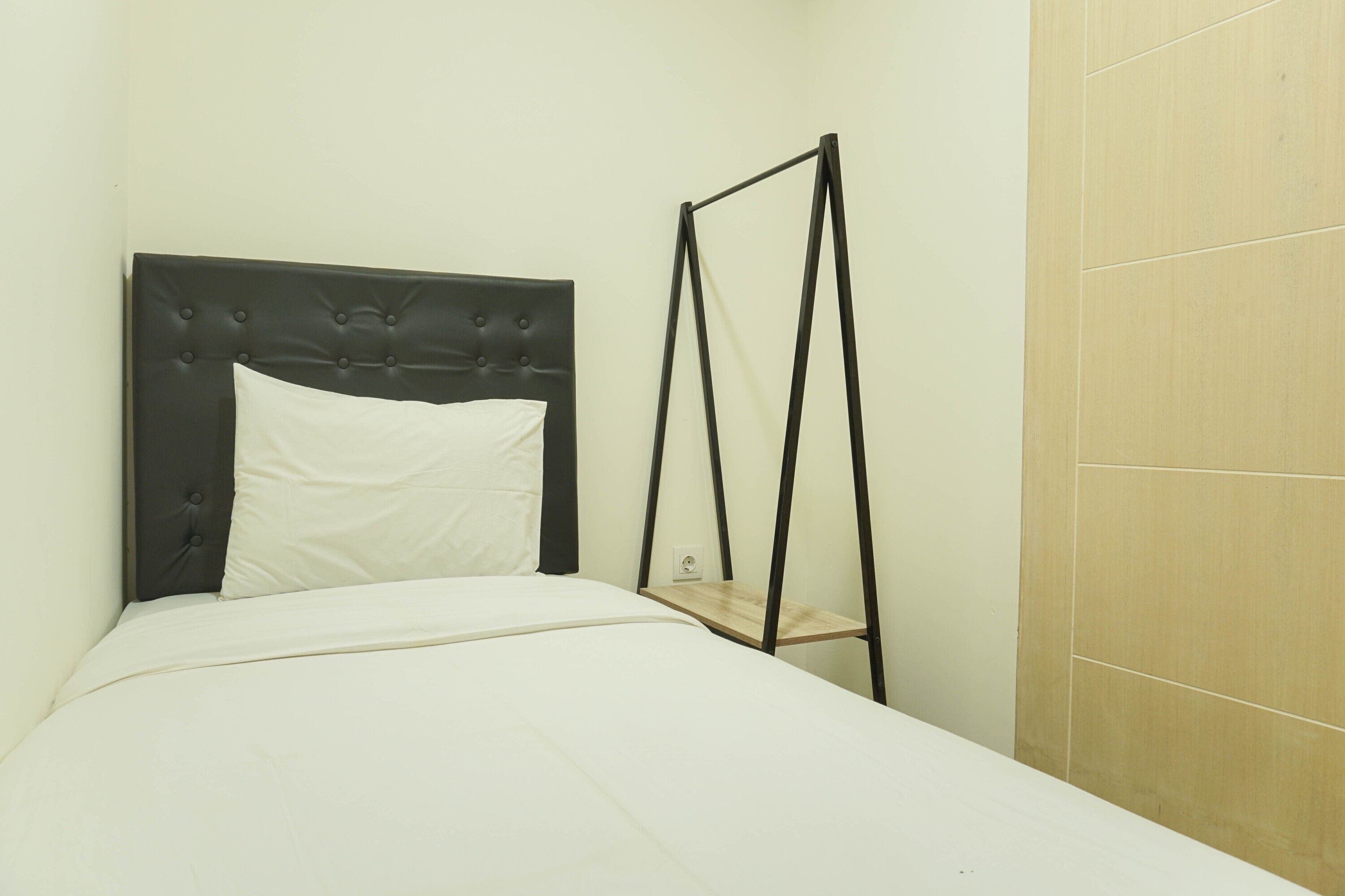 A neatly made bed with a tufted headboard, a white pillow, and a wooden shelf unit beside it.