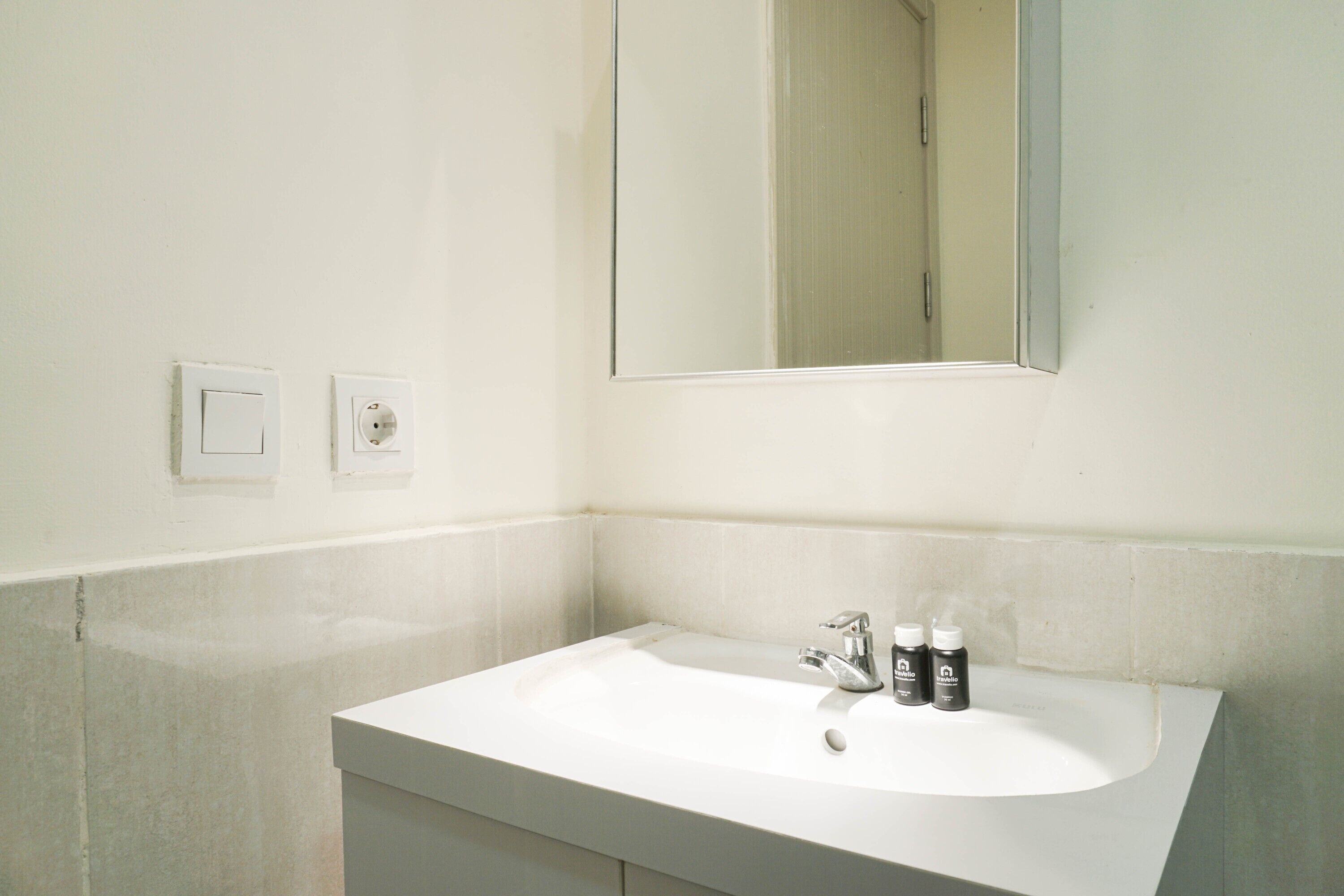 Une salle de bain avec un lavabo blanc, un miroir et deux interrupteurs sur le mur.
