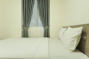 A neatly made bed with white linens and a wooden headboard, a window with sheer curtains, and a plain wall. - Brand New and Modern 2BR Meikarta Apartment (Cikarang)