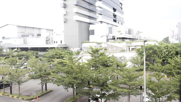 A modern building with multiple floors, a parking lot with trees, and a street with cars.