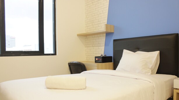 A hotel room with a bed, a desk, a chair, a window, and a brick wall. - Zest Studio Semi Apartment at The Lodge Paskal near BINUS University (Bandung)