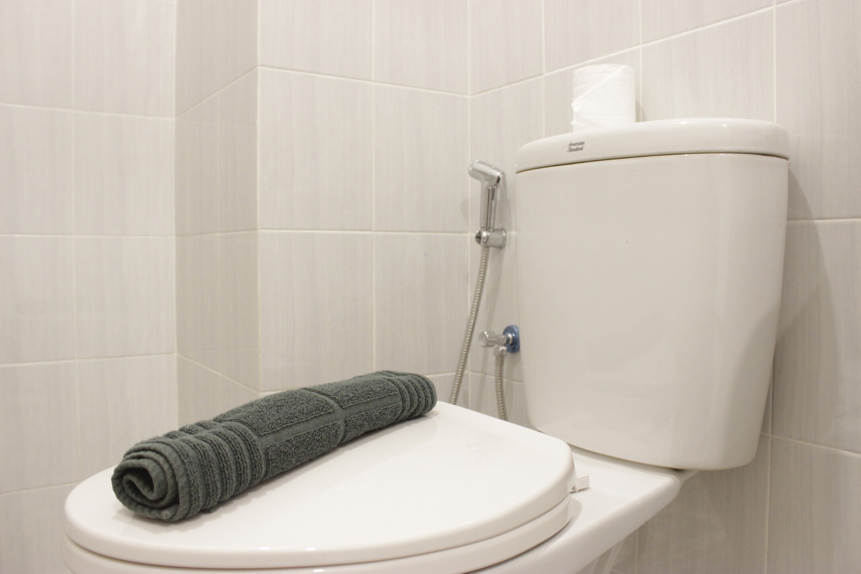 A toilet with a towel on it, a toilet paper holder, and a shower head.