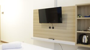 A modern hotel room with a mounted TV, a wooden shelf with toiletries, and a neatly made bed. - Zest Studio Semi Apartment at The Lodge Paskal near BINUS University (Bandung)