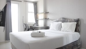 A modern hotel room with a large bed, a desk, and a chair. - Simply 2BR without Living Room Apartment at Parahyangan Residence (Bandung)