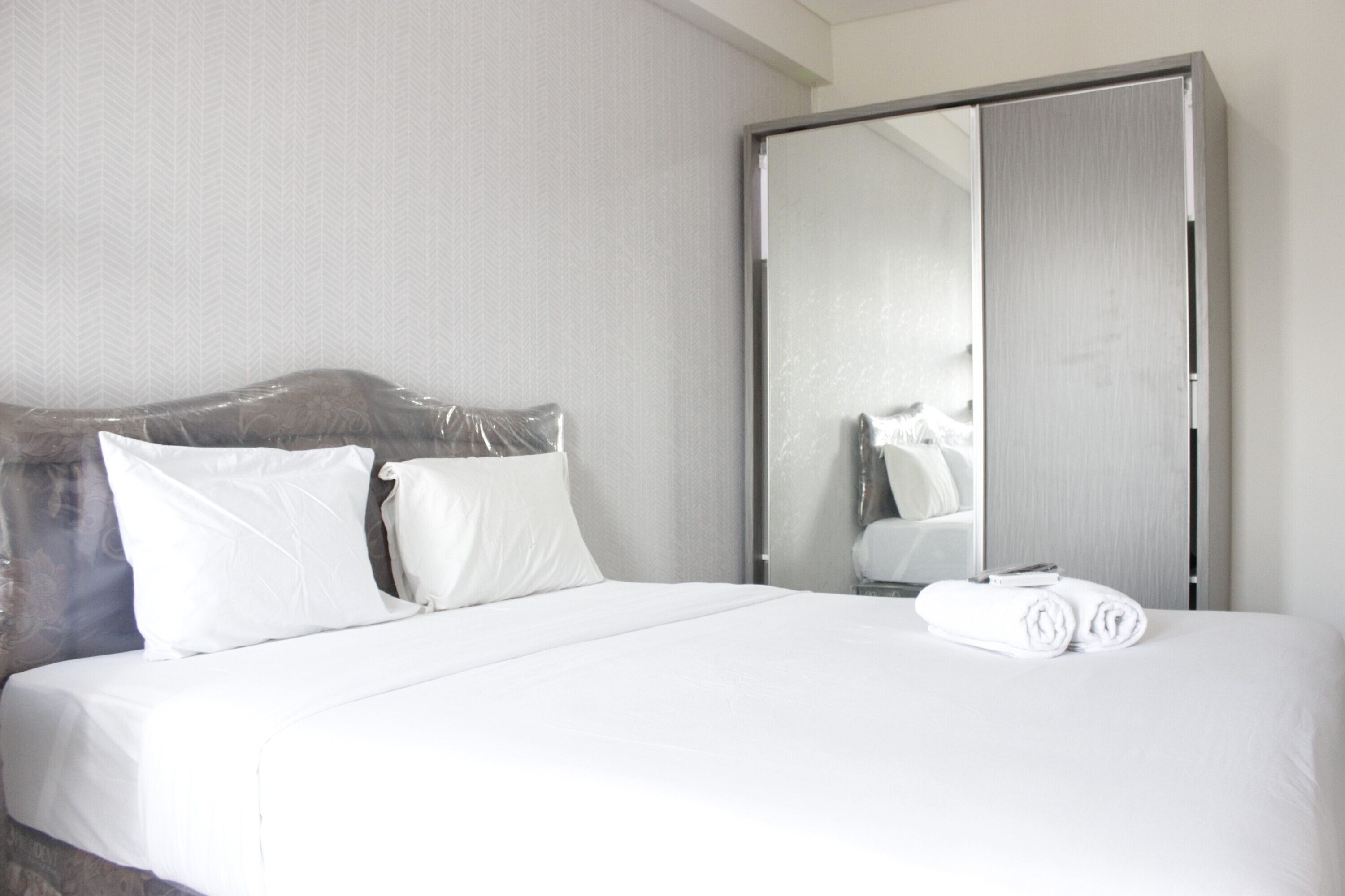 Une chambre d’hôtel avec un lit, du linge de lit blanc, une tête de lit en bois, un grand miroir et une armoire.