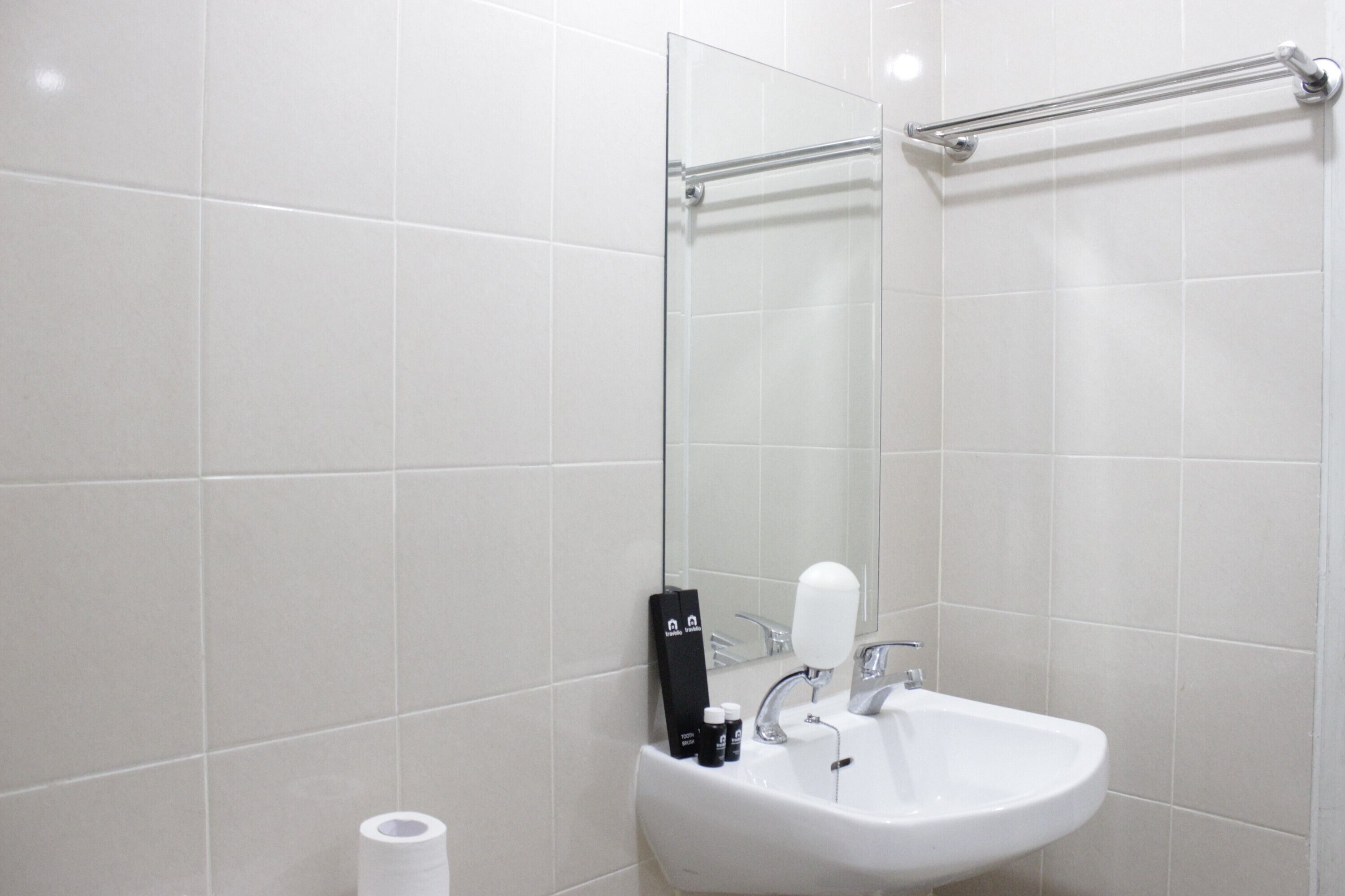Un baño moderno con azulejos blancos, cabina de ducha de vidrio, lavamanos blanco y secamanos.