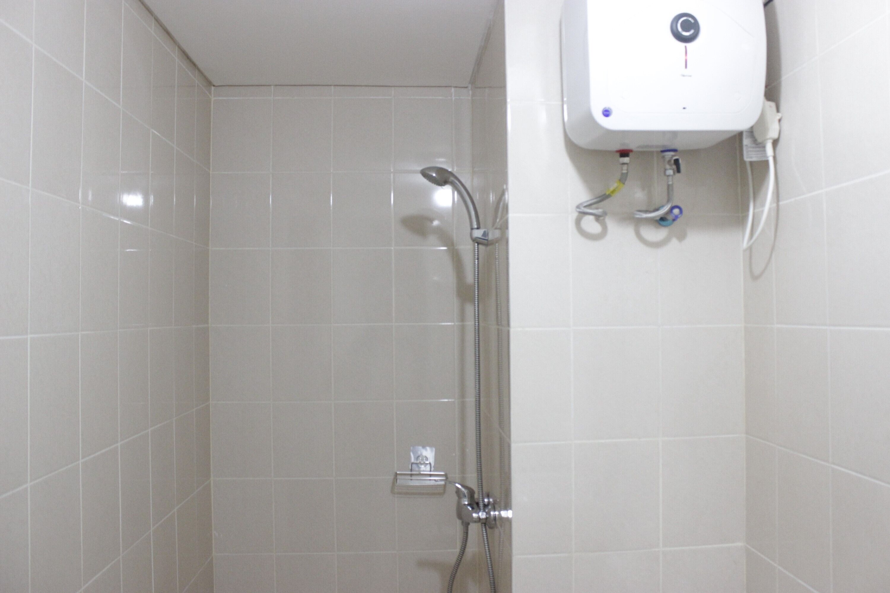 A bathroom with white tiled walls, a shower with a handheld showerhead, and a wall-mounted water heater.