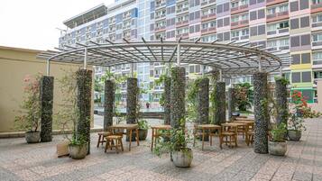 Ein Außenbereich mit Tischen und Stühlen, umgeben von Kübelpflanzen und einer Pergola-Konstruktion aus Metall.