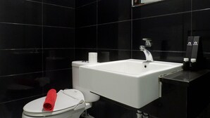 Un baño con inodoro y lavamanos blancos, y una pared revestida de baldosas negras.