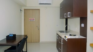 Une cuisine compacte avec une porte en bois, une petite table à manger avec des chaises, un évier encastré et un climatiseur fixé au mur.