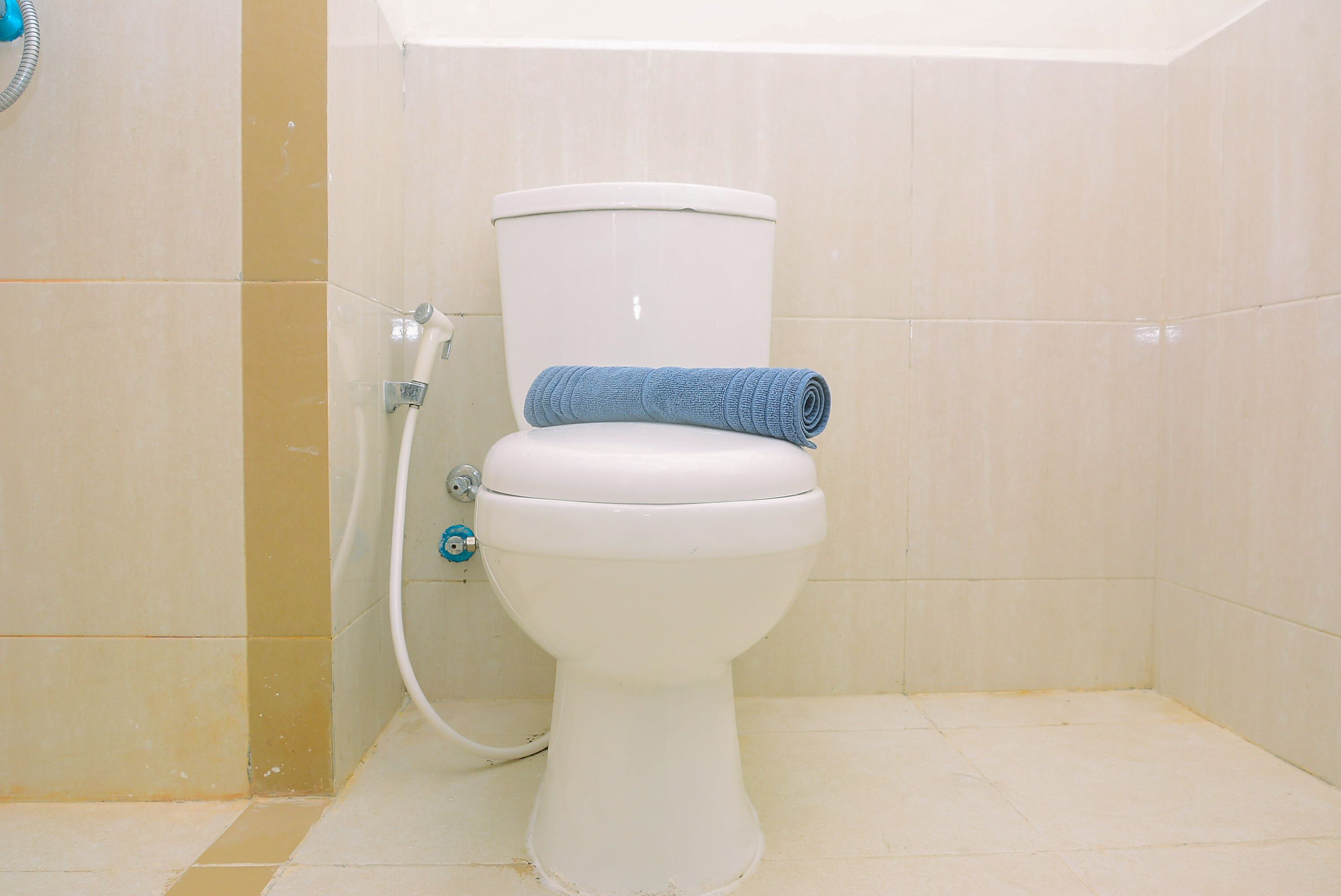 A white toilet with a blue towel on top, a showerhead, and beige tiled walls.