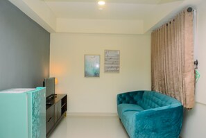 Un salon avec un canapé de couleur turquoise, un téléviseur posé sur un meuble et deux œuvres d’art encadrées accrochées au mur.