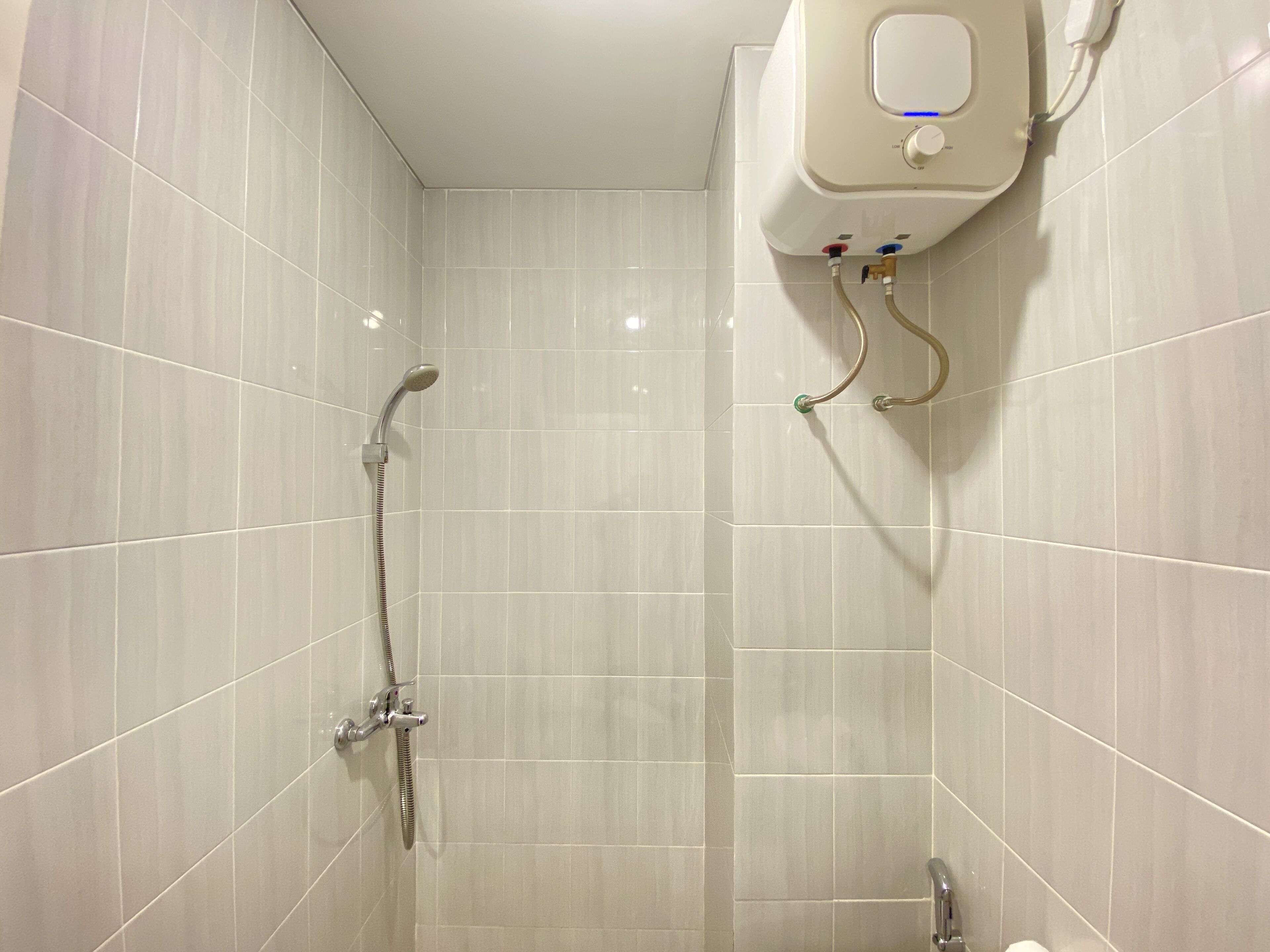 A modern bathroom with white tiles, a shower with a handheld showerhead, and a wall-mounted faucet.
