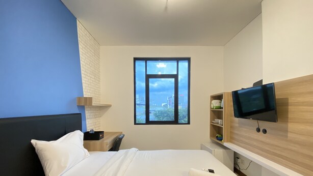 Habitación de hotel moderna con una cama grande, un televisor montado en la pared, una ventana con vistas a la ciudad y un pequeño escritorio con lámpara.