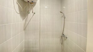 Un baño con paredes de azulejos blancos, una ducha con cabezal de ducha manual y un grifo empotrado.