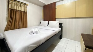 Quarto de hotel com cama, cortinas brancas, cabeceira de madeira e mesa de cabeceira pequena.