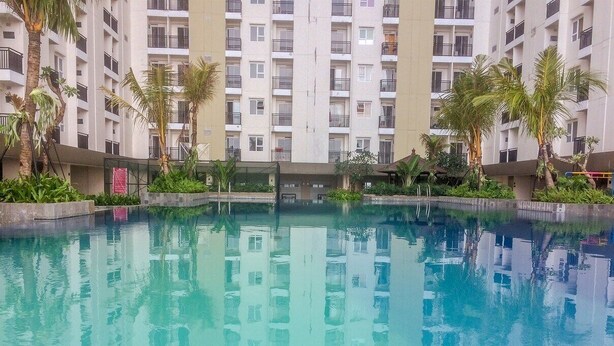 An indoor swimming pool with clear blue water, surrounded by a high-rise residential building with balconies. - Marvelous & Scenic 2BR at Jarrdin Cihampelas Apartment (Bandung)