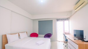 A hotel room with a bed, a desk with a TV, and two chairs.