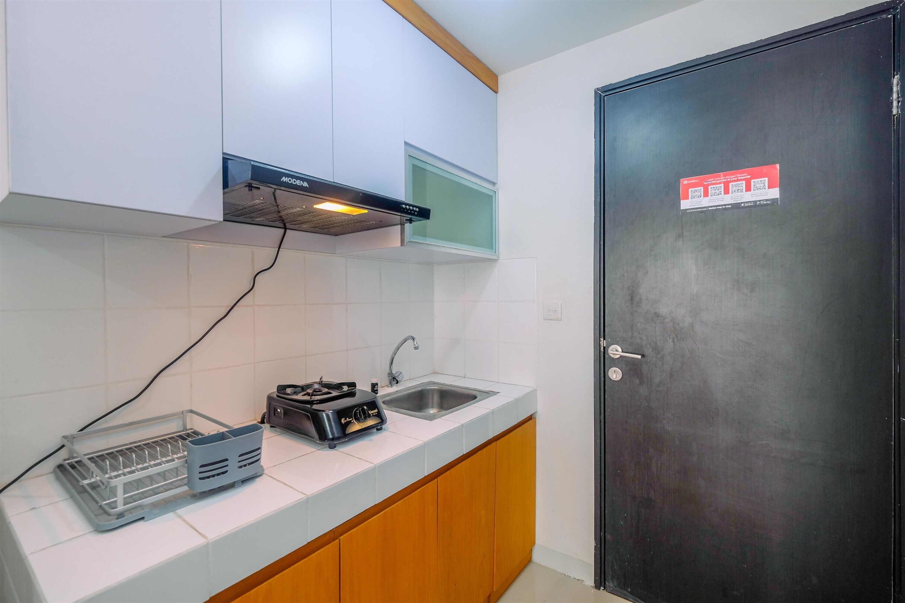 A kitchen with white cabinets, a black range hood, a sink, and a door with a QR code.