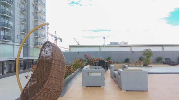 A rooftop terrace with a hanging chair, outdoor seating, and a view of a building under construction.